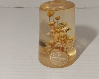 May include: A clear glass cylinder with a bouquet of dried white and yellow flowers inside. The cylinder has a gold label on the bottom that reads "Daisyglas Company Hand-Crafted".