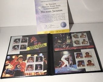 May include: A black album with a Michael Jackson stamp collection. The album features a certificate of authenticity from the Franklin Mint. The stamps feature images of Michael Jackson and the text "Michael Jackson" and "St. Vincent".