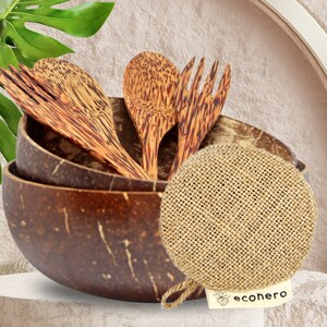 May include: A set of three brown coconut bowls with a brown coconut spoon and fork. The bowls are stacked on top of each other. A brown and beige woven scrubby is in front of the bowls. The scrubby has a white tag with the text "ecohero" on it.