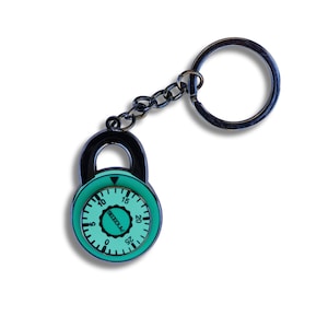 May include: A black combination lock keychain with a green dial. The dial has numbers from 0 to 25 and the word "SECURE" printed on it.