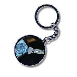 Puede incluir: Un llavero de metal negro con un dije redondo que presenta una huella digital azul y una linterna con detalles coloridos.