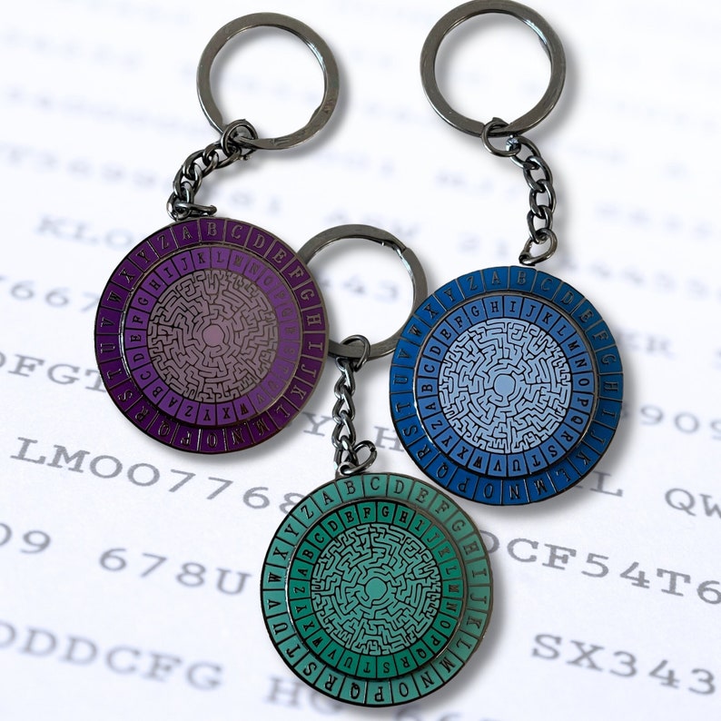 May include: Three keychains with circular metal charms featuring a maze design. The charms are purple, blue, and green with white letters around the edge spelling out the alphabet.