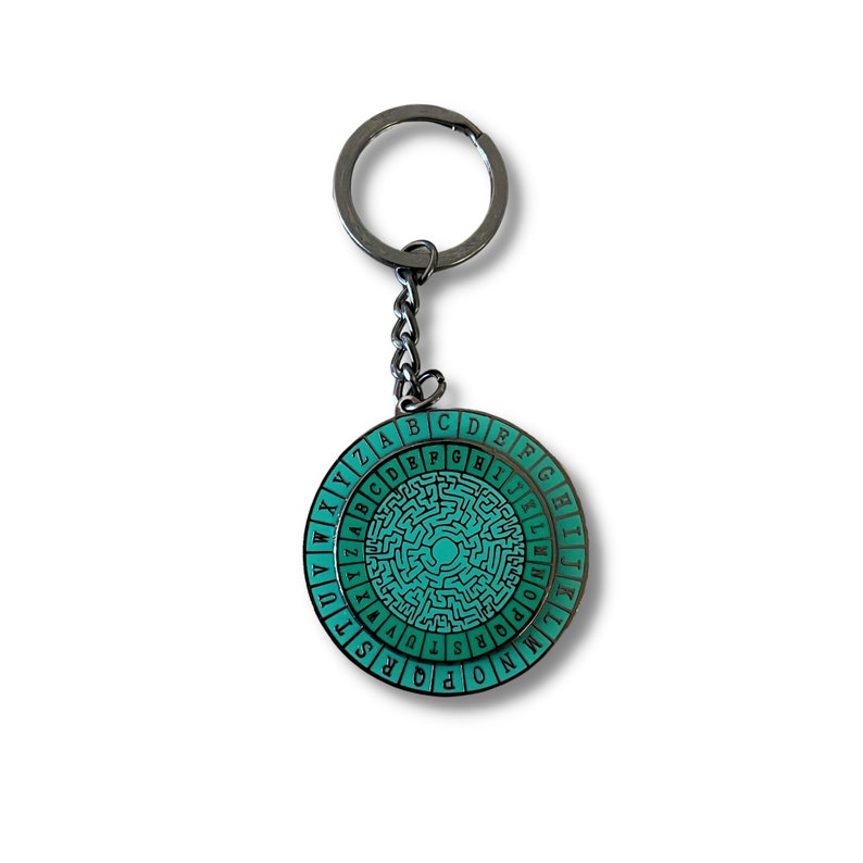 May include: A teal and black metal keychain with a circular design featuring a maze pattern and the alphabet around the edge.