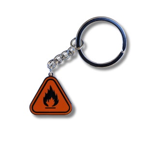May include: A silver keyring with a triangular charm. The charm is orange with a black flame symbol inside. The keyring is a great way to add a touch of personality to your keys.