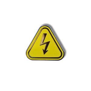 May include: A yellow triangle warning sign with a black lightning bolt inside. The sign is a metal pin.