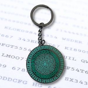 May include: A silver keychain with a round, green and black metal disc featuring a maze pattern and the letters of the alphabet around the edge.