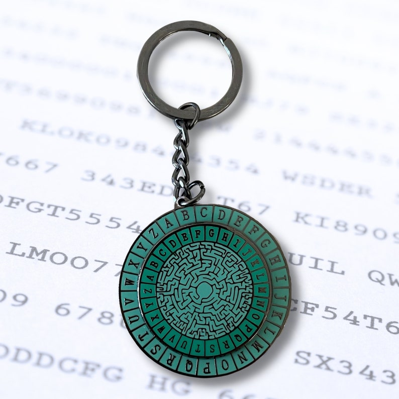 May include: A silver keychain with a round, green and black metal disc featuring a maze pattern and the letters of the alphabet around the edge.