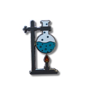May include: A silver enamel pin depicting a round-bottom flask with blue liquid and bubbles, held by a silver stand with a small flame underneath.