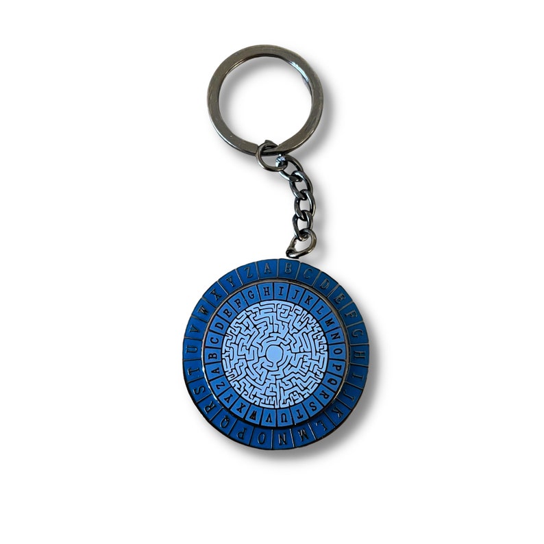 May include: A blue and white metal keychain with a circular design featuring a maze and the alphabet around the edge. The keychain has a silver metal ring.