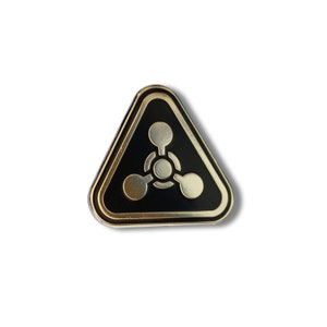 May include: A black triangle-shaped pin with a gold border and a gold symbol of three connected circles inside.