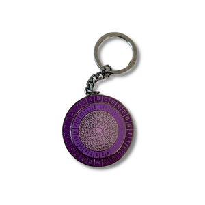 May include: A purple and silver metal keychain with a circular disc featuring a maze design and the alphabet around the edge.