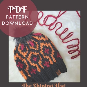 May include: A black, orange, and red knit hat with a faux fur pom-pom. The hat features a geometric pattern and the text "The Shining Hat" at the bottom. The image also includes the text "PDF PATTERN DOWNLOAD" in a circular shape.