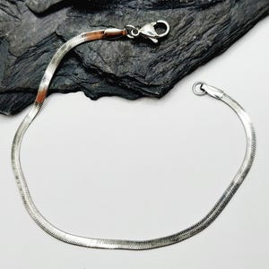 Op de afbeelding: Een zilveren slangenketting armband met een karabijn sluiting.