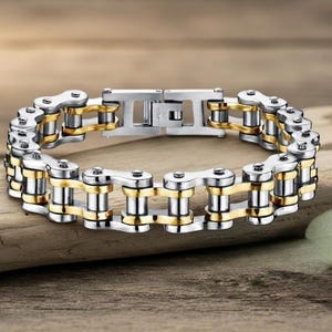 Puede incluir: Una pulsera de cadena de acero inoxidable y tono dorado. La pulsera presenta una serie de eslabones interconectados, con segmentos plateados y dorados alternos. El cierre es plateado y asegura la pulsera.