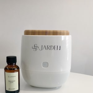 May include: White essential oil diffuser with a bamboo lid and a small brown bottle of "FRANGIPANE LOVE" essential oil. The diffuser has the word "JARDEN" printed on the front.