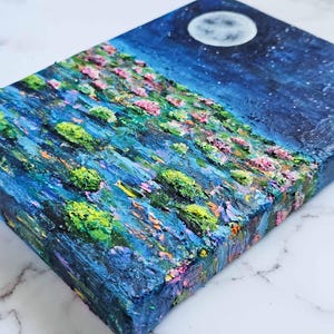 K&ouml;nnte beinhalten: Strukturiertes Acrylgem&auml;lde einer Nachtlandschaft mit Vollmond und Sternen. Das Kunstwerk zeigt einen H&uuml;gel mit rosa und gr&uuml;n strukturiertem Laub, gemalt mit dicken Pinselstrichen. Die Farbpalette umfasst Blau-, Gr&uuml;n-, Rosa- und Wei&szlig;t&ouml;ne.