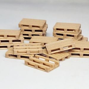 Puede incluir: Una colección de pequeñas paletas de madera de color marrón claro. Algunas están apiladas, otras dispersas, creando una escena industrial en miniatura. Las paletas tienen un diseño clásico con soportes horizontales y verticales.