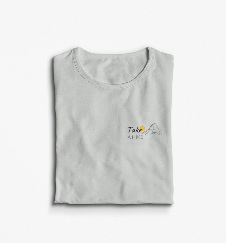 May include: A light gray t-shirt with a small graphic of a mountain and sun with the text "Take a Hike" printed on the front.