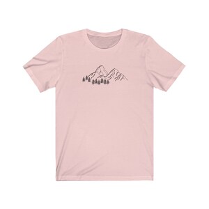 May include: A pink short-sleeved t-shirt with a black line drawing of mountains and trees on the front.