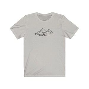 May include: A light gray t-shirt with a black line drawing of mountains and trees on the front.