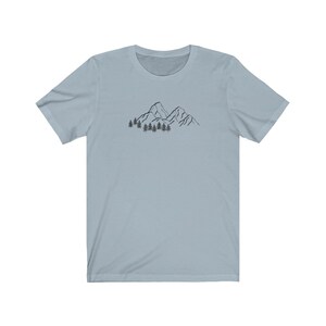 May include: A light blue t-shirt with a black line drawing of mountains and trees on the front.