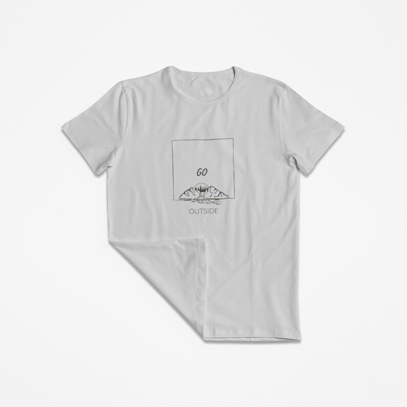 Peut inclure: Un t-shirt gris clair avec un motif graphique de montagnes et un soleil avec le texte "GO OUTSIDE" dans un cadre.