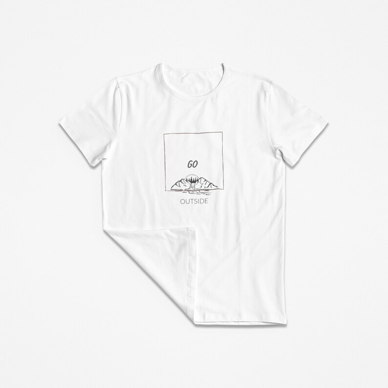 Peut inclure: T-shirt blanc avec un motif graphique noir et blanc de montagnes, un soleil et des arbres. Le texte "GO OUTSIDE" est imprim&eacute; sous le graphique.