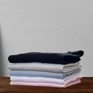 May include: A stack of folded t-shirts in various colors, including black, gray, light blue, white, and pink.