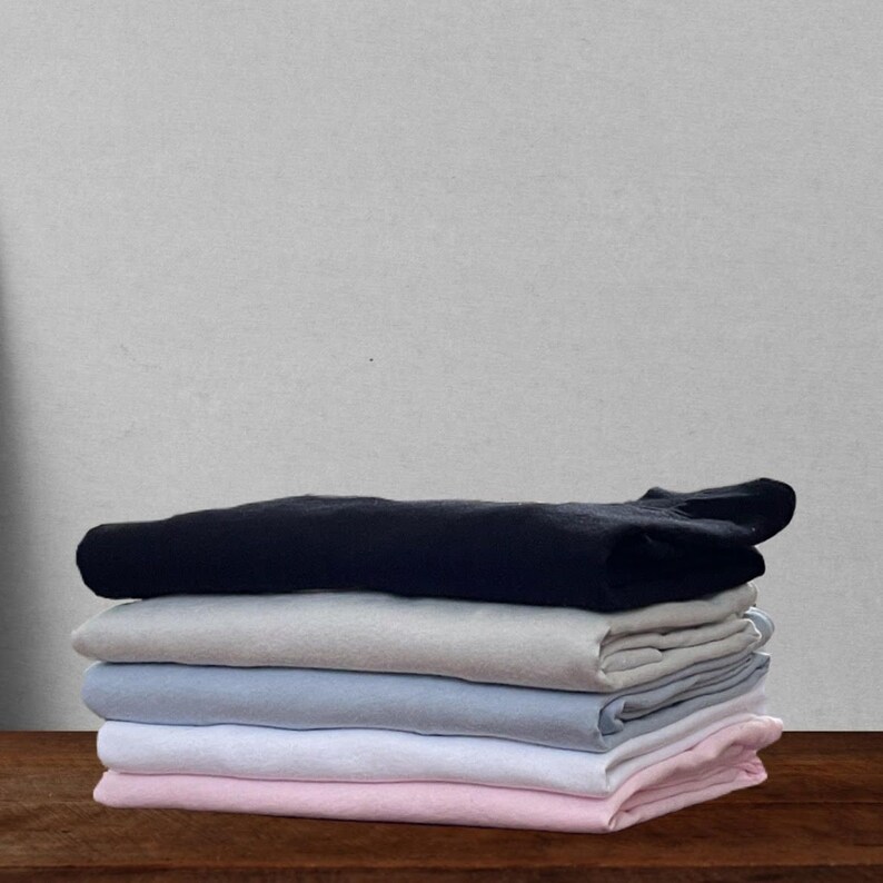 May include: A stack of folded t-shirts in various colors, including black, gray, light blue, white, and pink.