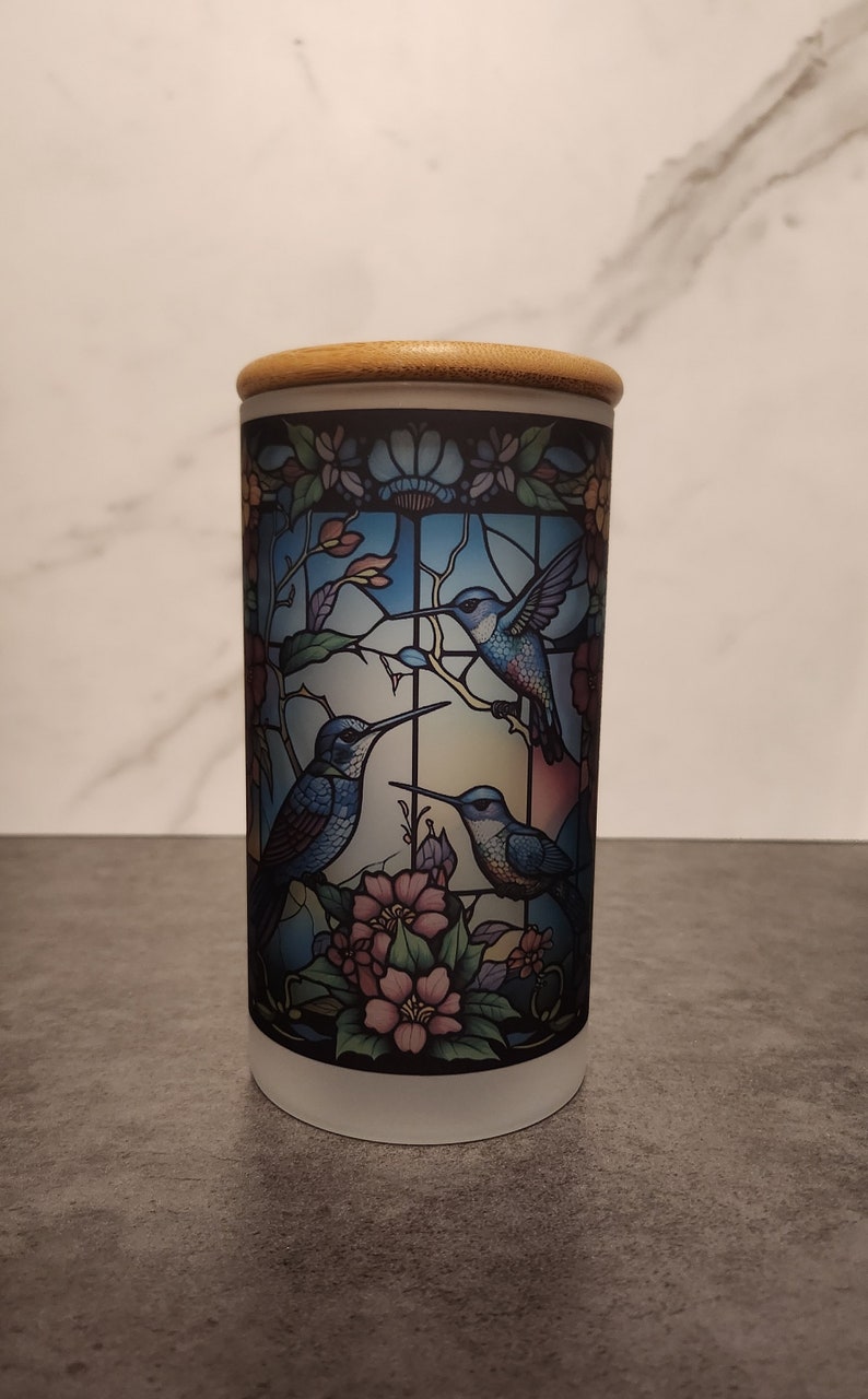 May include: A white ceramic jar with a wooden lid features a stained glass design of three blue hummingbirds and pink flowers.