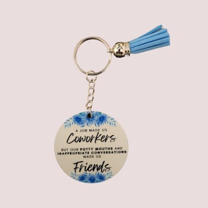 May include: A round keychain with a blue floral design and the text "A job made us coworkers but our potty mouths and inappropriate conversations made us friends". The keychain has a silver ring and a light blue tassel.