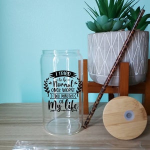 May include: A clear glass water bottle with a black and white graphic that reads "I tried -to be- Normal once worst two minutes of my life". The bottle has a bamboo lid and a straw.