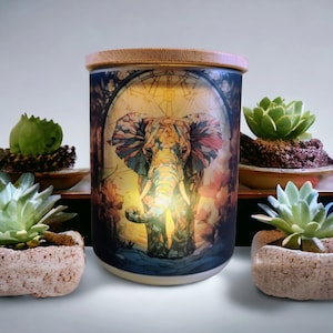 May include: A ceramic candle holder with a stained glass design of an elephant. The candle holder has a bamboo lid and is lit with a warm glow.