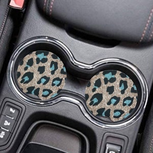 May include: Two round car coasters with a leopard print design in brown, black, and light blue. The coasters are in the cup holders of a car.