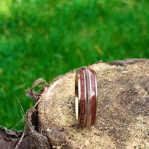 May include: A wooden ring with a brown and gold inlay. The ring is sitting on a tree stump.