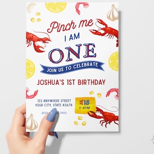 May include: A white birthday invitation featuring a red lobster, lemons, garlic, and corn. The text reads "Pinch me I am ONE. Join us to celebrate Joshua's 1st Birthday. 123 Anywhere Street, Your City, State 45678. 15 2-4PM. RSVP 66.7890."