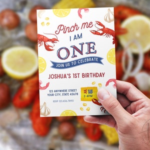 May include: A colourful invitation for a first birthday party with a crawfish boil theme. The invitation features a red crawfish, lemons, corn, garlic, and the text "Pinch me I am ONE. Join us to celebrate Joshua's 1st Birthday. July 15, 2-4PM."