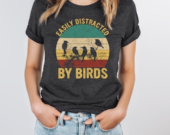 May include: Dark grey heather t-shirt with a vintage-style graphic of a sunset and birds. The text "Easily Distracted By Birds" is printed on the shirt.