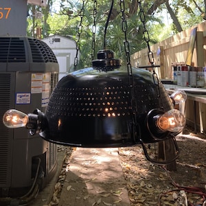 May include: Black, industrial-style hanging pendant light with three exposed Edison bulbs. The light fixture is suspended by chains and has a perforated shade. The image includes the text "#67" in the upper left corner.