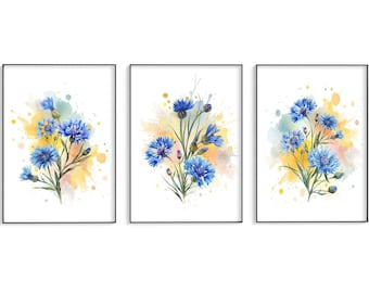 May include: Set of three framed art prints featuring watercolor paintings of blue cornflowers. Each print showcases a bouquet of flowers against a backdrop of yellow, blue, and orange paint splatters. The frames are black.