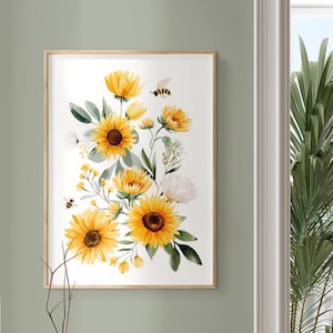 May include: A framed watercolour print of sunflowers and bees. The artwork displays bright yellow sunflowers with green leaves and white flowers, set against a white background. The frame is a light brown colour, and the overall theme is nature and floral.