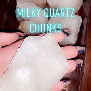Puede incluir: Una colección de trozos de cuarzo lechoso en un recipiente de vidrio transparente. El texto "MILKY QUARTZ CHUNKS" se muestra en la imagen.