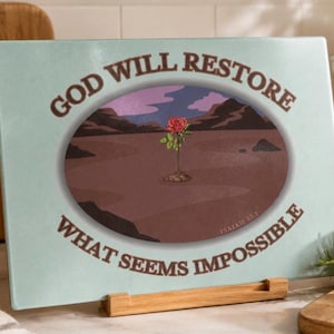 Könnte beinhalten: Ein rechteckiges Glasschneidebrett mit hellblauem Hintergrund und einer ovalen Illustration einer einzelnen roten Rose in einer Wüstenlandschaft. Der Text "GOD WILL RESTORE WHAT SEEMS IMPOSSIBLE" ist in brauner Schrift um das Oval gedruckt.