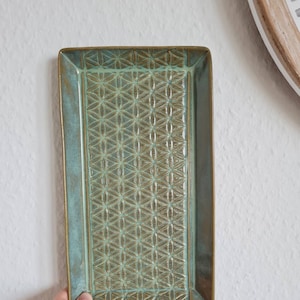 Könnte beinhalten: Ein rechteckiges Keramik-Serviertablett mit grüner Glasur und einem erhabenen geometrischen Muster in Braun. Das Tablett hat einen leicht erhöhten Rand.