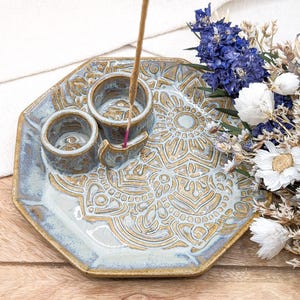 May include: A ceramic incense holder with a blue and gold mandala design. The holder has three small bowls for incense cones and a central stand for a stick incense.
