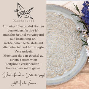 K&ouml;nnte beinhalten: Ein Keramik-Teller mit detailliertem goldenem Mandala-Design auf hellblauem Hintergrund. Der Teller ist von Trockenblumen und deutschem Text umgeben, darunter "Gl&uuml;cksvogel" und eine Nachricht &uuml;ber Artikel auf Bestellung.