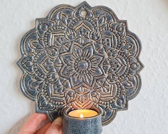 May include: A ceramic wall-mounted candle holder with a blue and gold mandala design. The holder has a small tealight candle holder attached to the bottom.