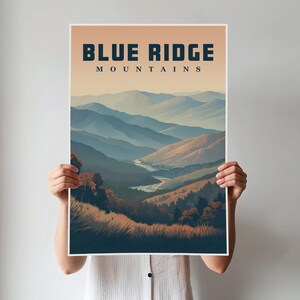 May include: A poster featuring the text "BLUE RIDGE MOUNTAINS" in navy blue, above a landscape painting of layered blue mountains, a river, and autumn-coloured trees. The poster is held by a person.