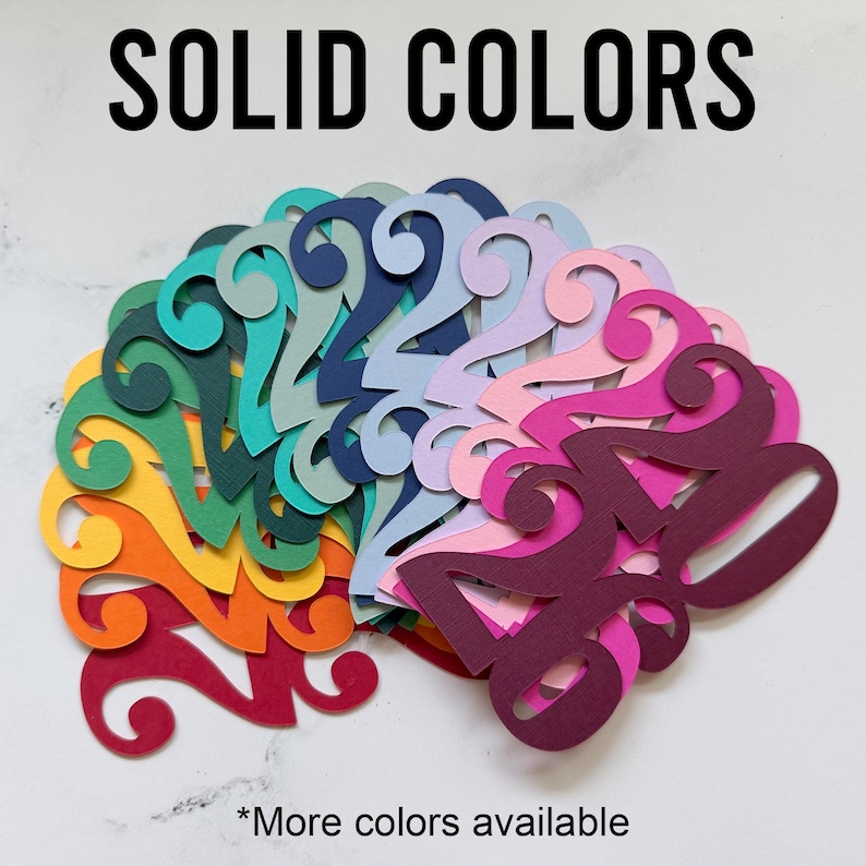 May include: A collection of colorful paper cutouts in various solid colors, arranged in a fan shape. The cutouts are in shades of green, blue, yellow, orange, pink, and purple. The text "SOLID COLORS" is at the top, with "*More colors available" at the bottom.