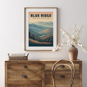 May include: A framed art print depicting the Blue Ridge Mountains. The image shows a layered landscape of blue and tan mountains under a warm sky. The words "BLUE RIDGE MOUNTAINS" are printed at the top of the artwork.